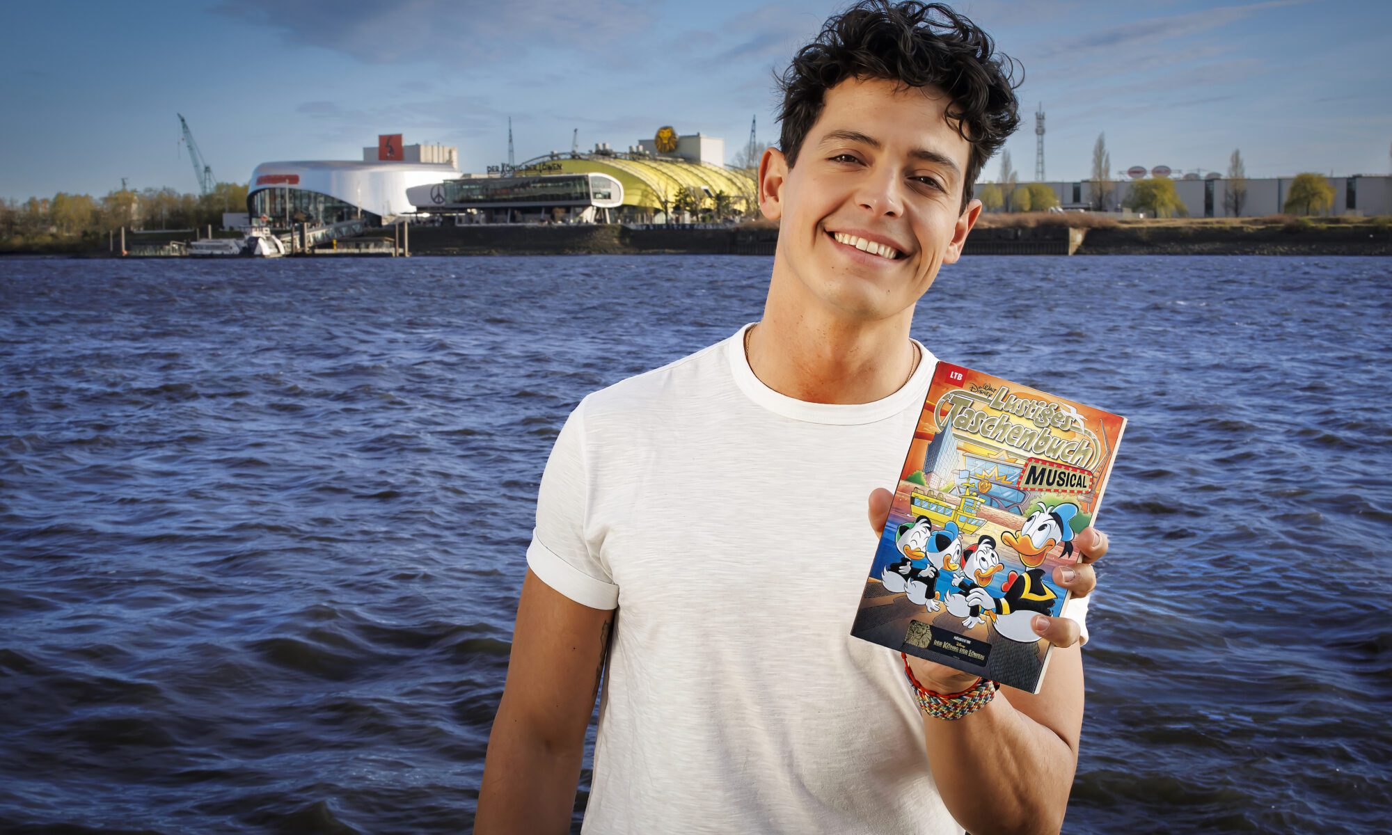 Simba-Darsteller Gonzalo Campos blättert freudig im neuen LTB Musical vor der Kulisse des Stage Theaters.