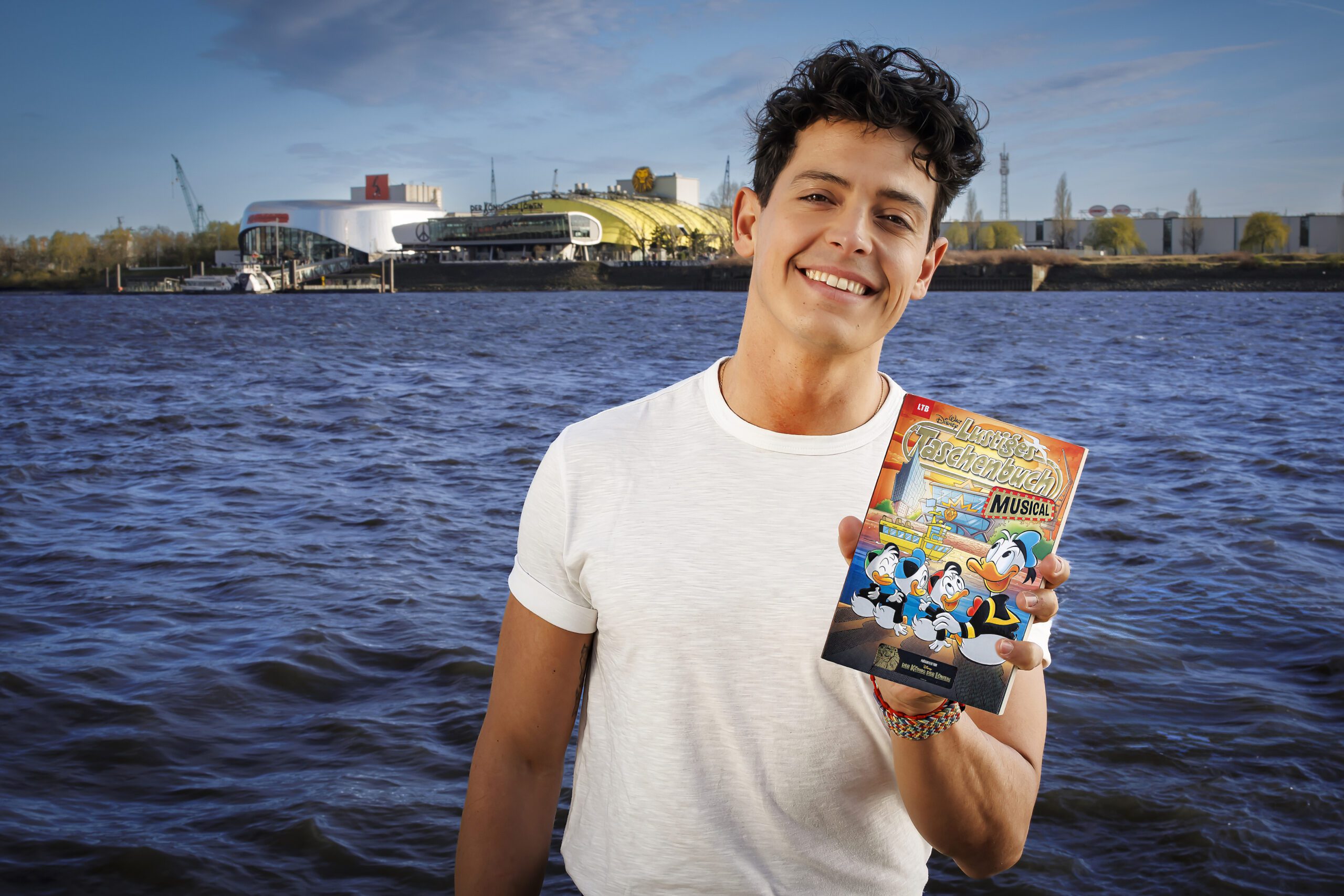 Simba-Darsteller Gonzalo Campos blättert freudig im neuen LTB Musical vor der Kulisse des Stage Theaters.